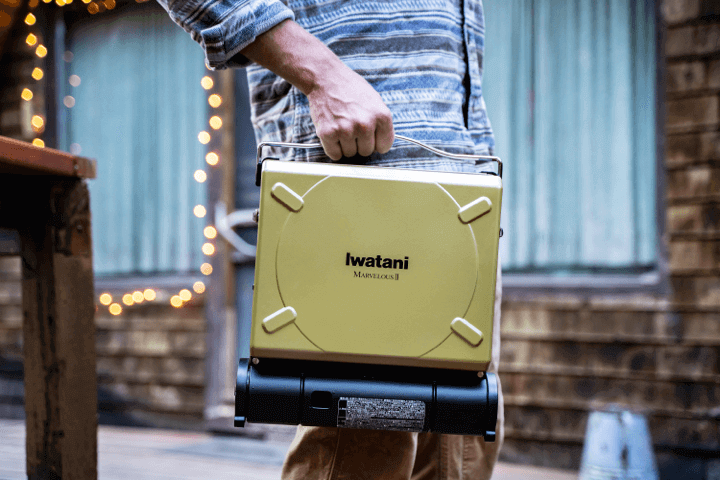 person holding a portable gas powered Iwatani grill.
