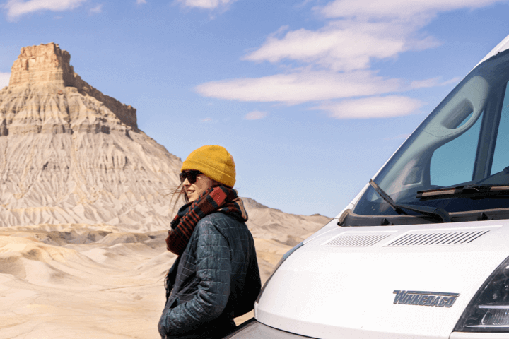 woman standing in front of RV wearing a yellow beanie, red scarf, and winter coat with shale 